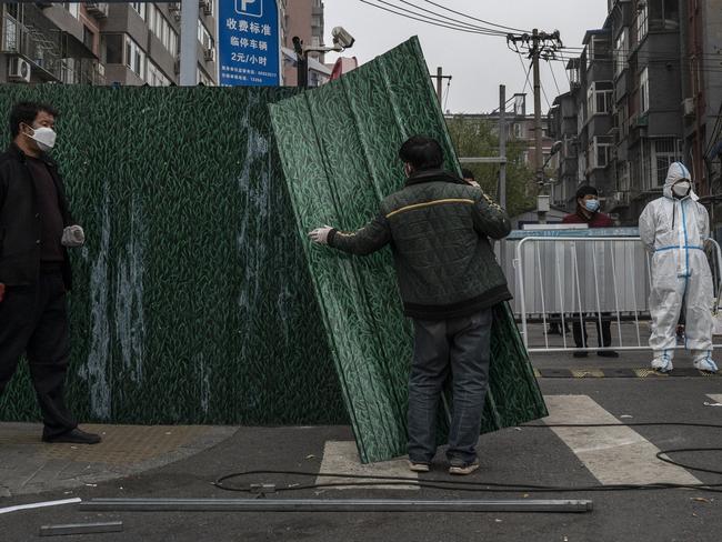 BEIJING, CHINA - NOVEMBER 24: An epidemic control worker wears a protective suit as he watches workers erect a metal barrier fence outside a community under lockdown to prevent the spread of COVID-19 on November 24, 2022 in Beijing, China. China recorded its highest number of COVID-19 cases since the pandemic began Wednesday, as authorities stuck to their strict zero tolerance approach: containing the virus with lockdowns, mandatory testing, mask mandates, and quarantines as it struggles to contain outbreaks. In an effort to try to bring rising cases under control, the government last week closed most stores and restaurants for inside dining, switched schools to online studies, and asked people to work from home. (Photo by Kevin Frayer/Getty Images)