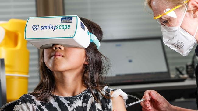 COMMERCIAL-  Nyomi  Meth 9, with a Smileyscope headset about to be vaccinated by nurse Maryanne Attard, Unit Manager at the Adelaide Women and Children Hospital Vax Clinic.IMAGE/Russell Millard