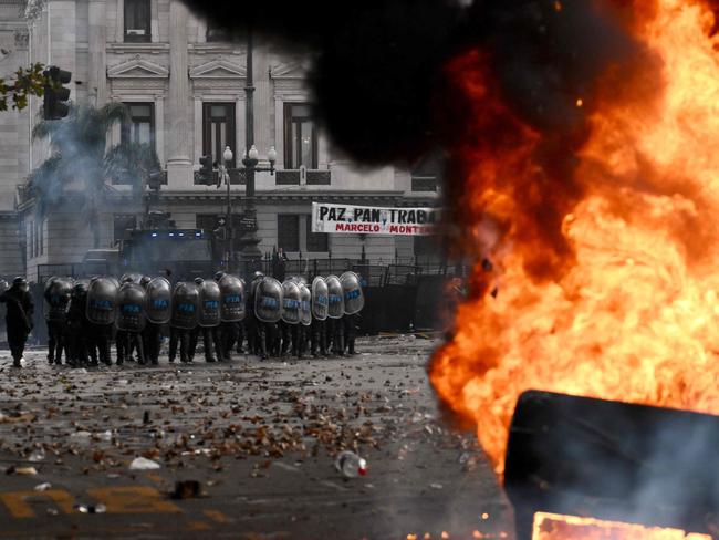 Anti-riot police officers stand guard behind a Cadena 3 radio station car on fire during a protest outside the National Congress in Buenos Aires on June 12, 2024. Argentine senators are discussing a key reform package for the ultra-right-wing president Javier Milei, in a session marked by strikes and demonstrations in front of Congress. (Photo by Luis ROBAYO / AFP)