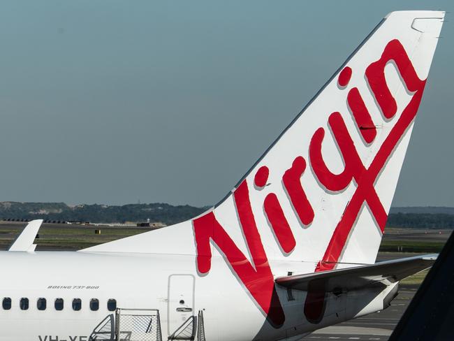 A man sits at a cafe in front of a Virgin Australia aircraft at Sydney Airport, Sydney, Friday, June 19, 2020. (AAP Image/James Gourley) NO ARCHIVING