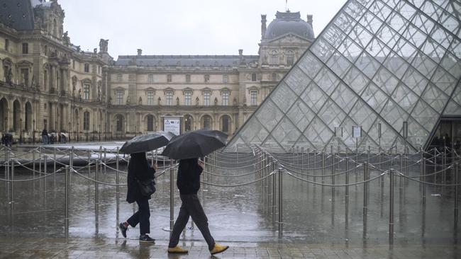 People walk by the now-closed Louvre museum, in Paris, on Sunday.