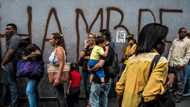 People queue next to a wall with a graffiti reading ‘Hunger’ in Caracas, Venezuela, on July 23, 2018 as the country saw hyperinflation reach epic proportions. Picture: Juan Barreto/AFP