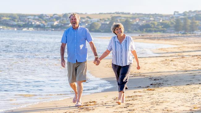 Happy senior couple embracing and holding hands walking on empty beach at sunset. Active healthy elderly woman and man on a romantic walk by the sea. Aging together and retirement lifestyle concept. Middle-aged early retirees generic