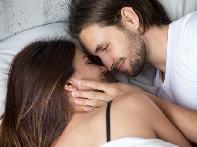 Happy affectionate young couple lying in bed face to face, smiling lovers enjoying intimacy and pleasant morning together, man tenderly touching woman, love and sensuality concept, close up top view