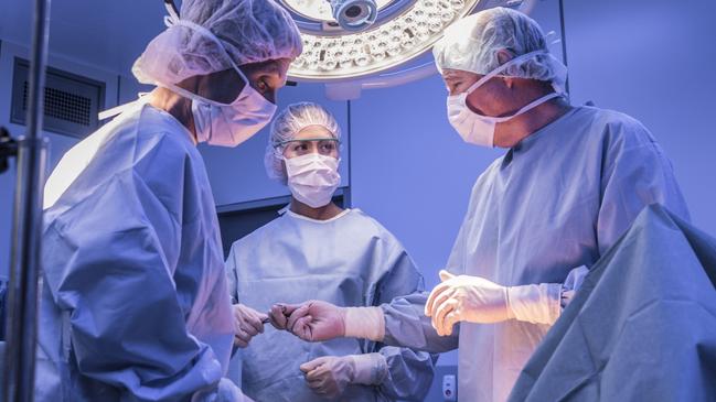 Doctors wearing surgical masks and gowns performing an operation on patient in hospital operating theater.