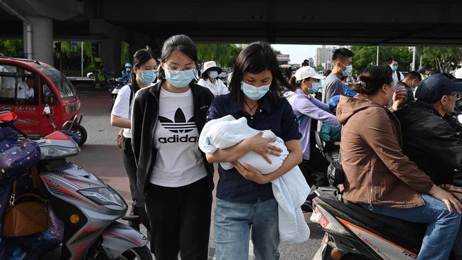 A woman carries a baby through a busy intersection in Beijing this month, days after China announced it would allow couples to have three children. Picture: Greg Baker/AFP