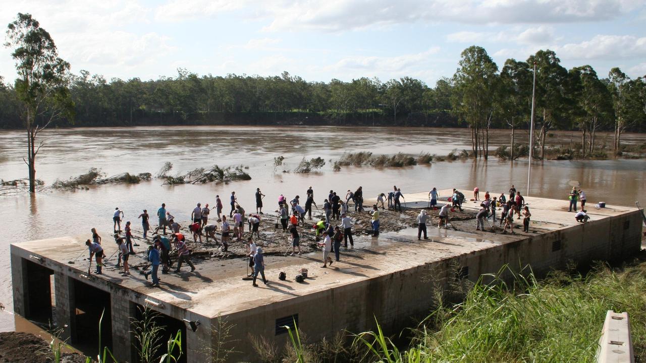 People scraping mud from the roof of the Centenary Rowing Club's shed.