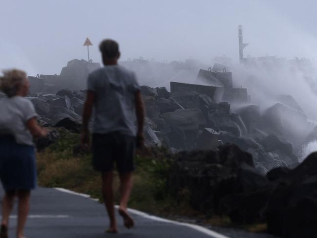 Residents take a morning walk as massive waves, stirred by tropical cyclone Alfred, crash against the North Wall in Ballina Picture: David Gray/AFP