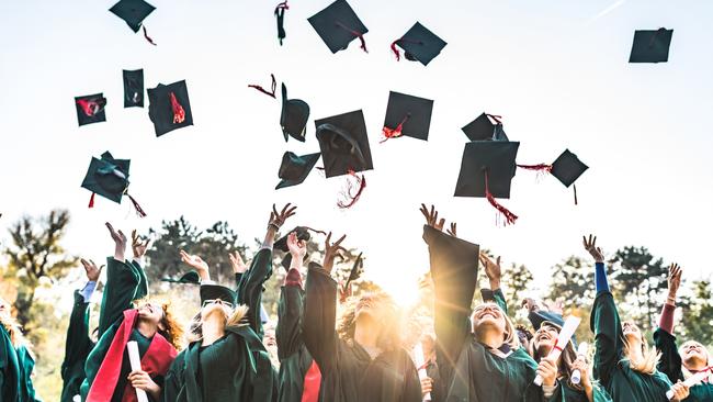 Large group of happy college students celebrating their graduation day outdoors while throwing their caps up in the air.