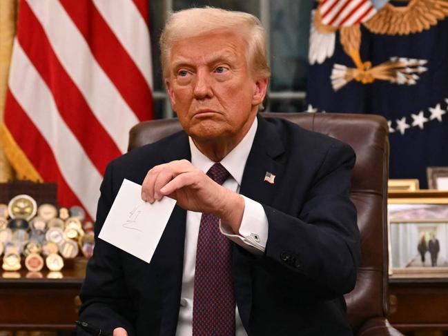 US President Donald Trump holds up outgoing President Joe Biden's letter as he signs executive orders in the Oval Office of the WHite House in Washington, DC, on January 20, 2025. (Photo by Jim WATSON / POOL / AFP)