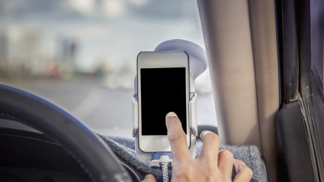 Man driving and using a phone secured in a cradle. Picture: iStock.