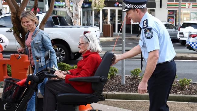 Chief Superintendent Mark Wheeler assists an elderly woman after her mobility scooter got caught on a plastic barrier at the Griffith St border checkpoint. Picture: STEVE HOLLAND