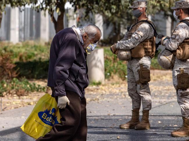 An elderly man wears face mask and gloves as he walks past Chilean soldiers outside Del Carmen Hospital in Santiago. Picture: Martin Bernetti