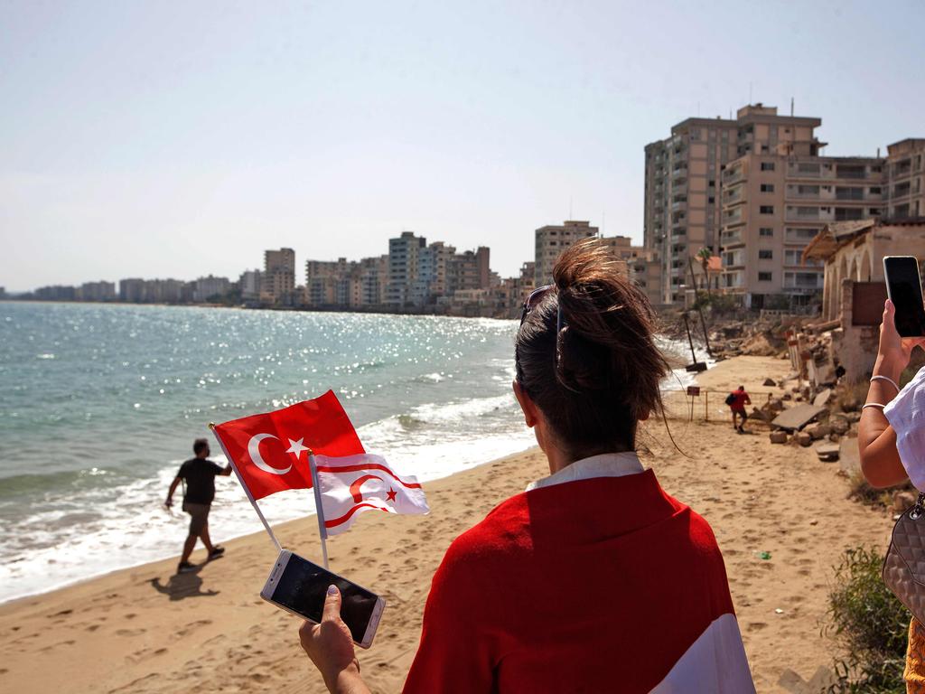 A woman holds the flags of Turkey and the self-proclaimed Turkish Republic of Northern Cyprus as tourist return to Varosha. Picture: Birol Bebek / AFP