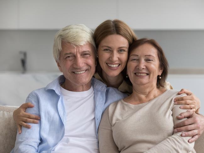 Happy pretty adult woman hugging positive older parents with love, care, support, affection, looking at camera, smiling, enjoying meeting at home, good relationship, bonding. Family portrait; senior couple early inheritance generic