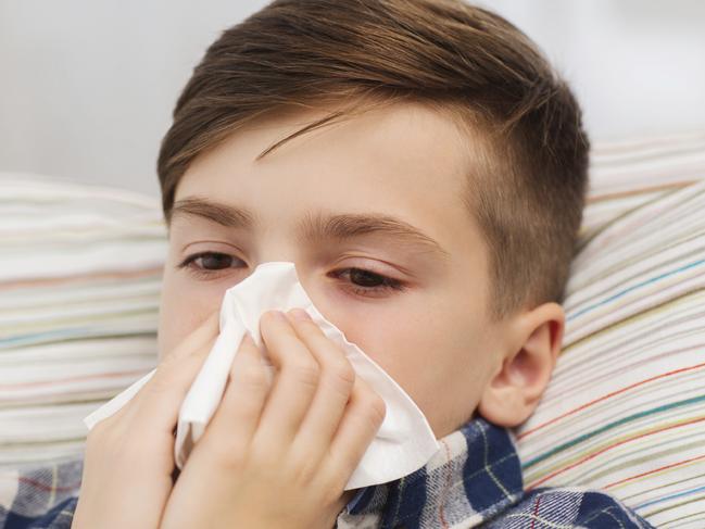 childhood, healthcare, rhinitis, people and medicine concept - ill boy with flu lying in bed and blowing his nose at home