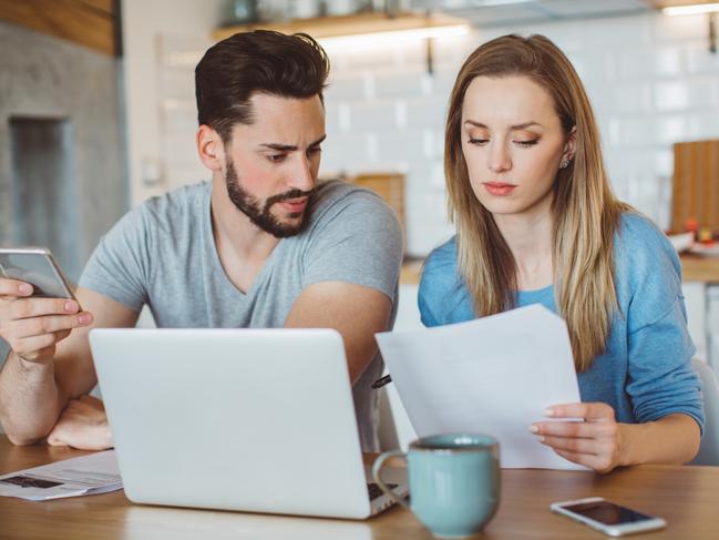 Young couple worried about their finances at home. They are wearing pajamas and drinking first coffee of the day at the kitchen.