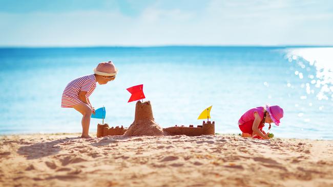 Ultimate list for family fun in Adelaide. Boy and girl playing on the beach on summer holidays. Children building a sandcastle at sea.