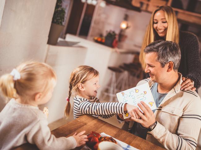 Happy family celebrating father's day with little girls surprising father with handmade card