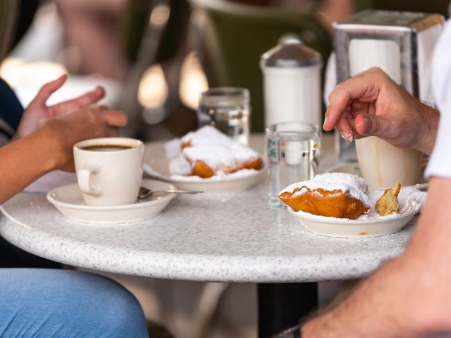 ESCAPE:  Closeup of couple sitting outside at sidewalk cafe by table drinking chicory coffee and eating deep fried beignet donut powdered with sugar Picture: Istock