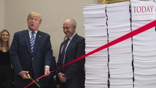 Donald Trump cuts a red tape tied between stacks of papers representing the government regulations of the 1960s and those of today in the White House last week. Picture: AFP.