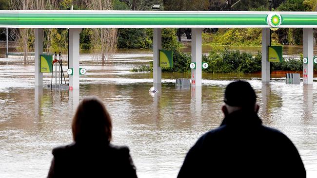 People stand next to a flooded petrol station in the Camden suburb of Sydney on Sunday. Suncorp expects a large number of insurance claims this week. Picture: AFP