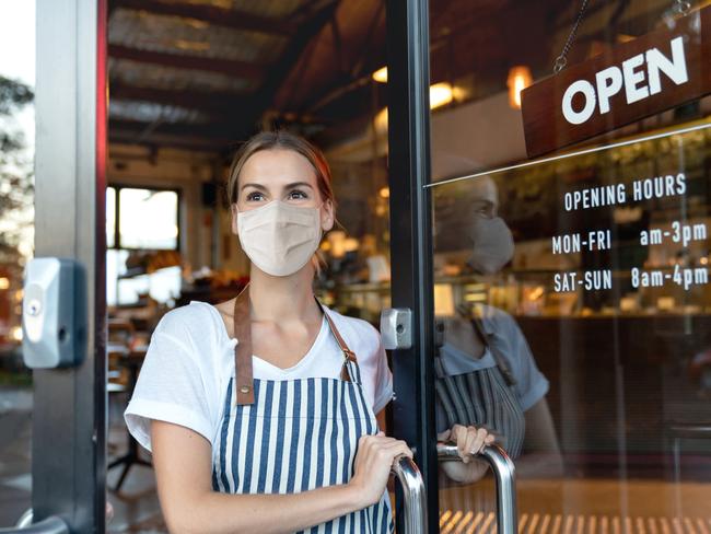 Happy business owner opening the door at a cafe wearing a facemask to avoid the spread of coronavirus ÃÂ¢Ãâ¬Ãâ reopening after COVID-19 concepts