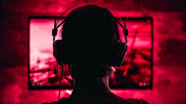 Woman wearing headphones playing video games late at night. Video games, gaming, screen time, kids and technology, headphones, generic