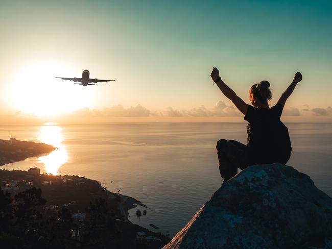 A teenage girl watches an airplane flying over the sea coast at sunrise.