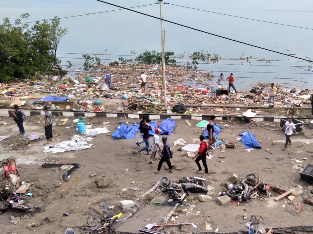 People walk past dead bodies a day after a tsunami hit Palu, on Sulawesi island. Picture: AFP