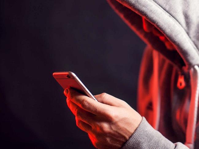 Man wearing hoody sweater with mobile phone in hands. Crime and hacking concept; scam generic.