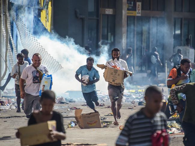 TOPSHOT - People run with merchandise as crowds leave shops with looted goods amid a state of unrest in Port Moresby on January 10, 2024. A festering pay dispute involving Papua New Guinea's security forces on January 10 sparked angry protests in the capital, where a crowd torched a police car outside the prime minister's office. By Wednesday afternoon pockets of unrest had spread through the capital Port Moresby, with video clips on social media showing crowds looting shops and stretched police scrambling to restore order. (Photo by AFP)