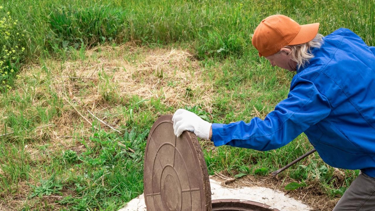 A plumber opens a manhole cover on a concrete well. Inspection and maintenance of water and sewer wells.