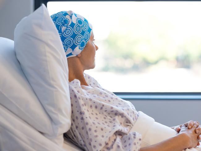 Young woman in bed suffering from cancer. Thoughtful woman battling with tumor looking out of window. Young patient with blue headscarf recovery in hospital on bed.