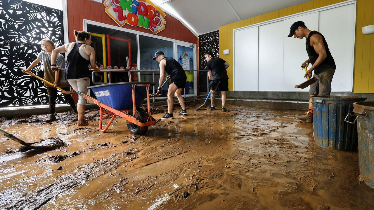 Ellis Beach Bar and Grill staff members scrape up inches of thick mud from the floor after debris caused by flooding rain tore through the popular beachside eatery on Sunday. Picture: Brendan Radke