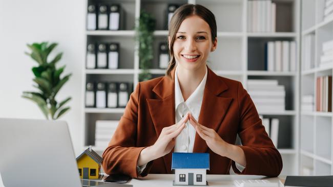 Female real estate agent is use hands to protect red roof for the concept of real estate investment about house trading, purchase at desk in office;  woman property investing generic