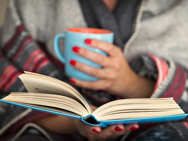 woman reading a book and holding a mug of hot beverage