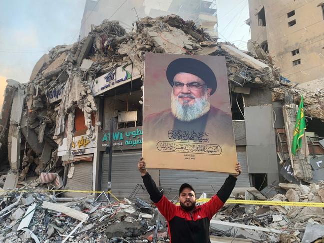 A man flashes a portrait of slain Hezbollah chief Hassan Nasrallah in front of the rubble of a building at the site of an Israeli airstrike in Beirut's southern suburbs, on November 12, 2024, amid the ongoing war between Israel and Hezbollah. (Photo by AFP)