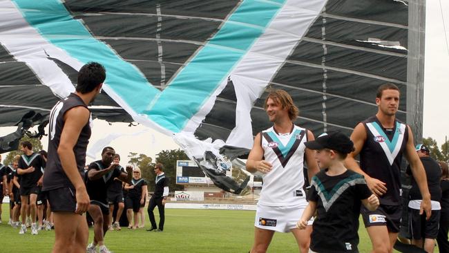 Jumper designer Lucy Burford, front, leads Port Adelaide footballers Travis Boak and Domenic Cassisi wearing the then new home strip, with Jacob Surjan wearing the away guernsey, in 2010.