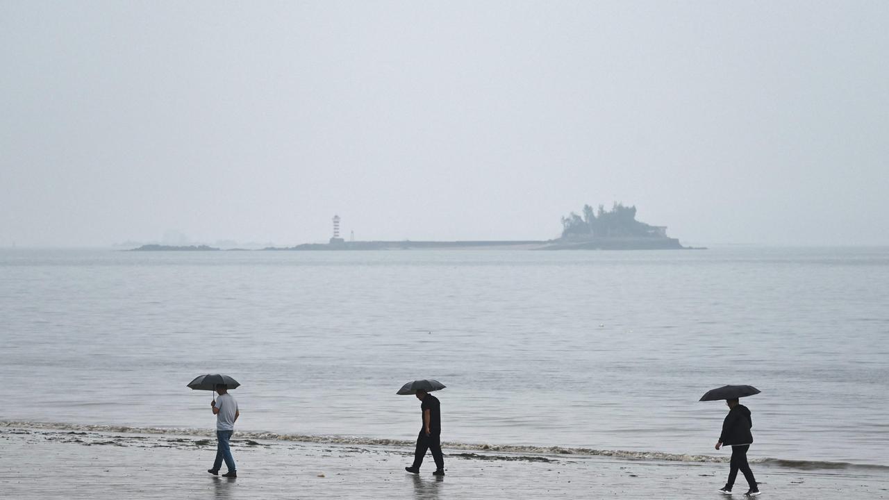 People walk with their umbrellas on a beach in Xiamen, where on a clear day the Taiwanese island of Kinmen (not pictured) can be seen, in southeast China's Fujian province on May 23, 2024. (Photo by Greg Baker / AFP)