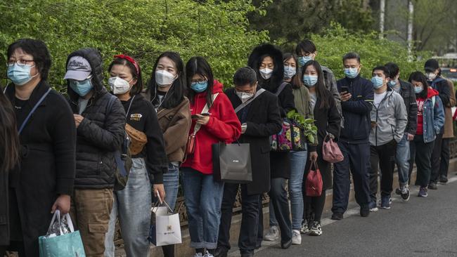 Commuters wear protective masks as they line-up and wait to board a public bus home in the central business district during rush hour in Beijing. Picture: Getty Images