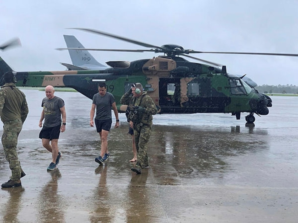 Australian Army soldiers from the School of Army Aviation walk with rescued community members on the flightline at RAAF Base Amberley. Picture: Australian Defence Department