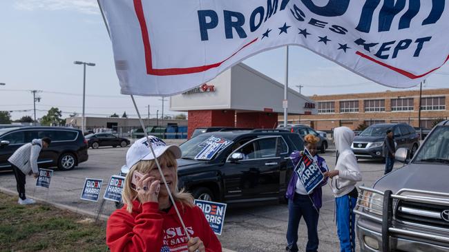 A supporter of US President Donald Trump walks by supporters of Democratic Presidential nominee Joe Biden, near the polling place, where residents waited in line to cast their vote during early voting in the US state of Ohio on October 6.