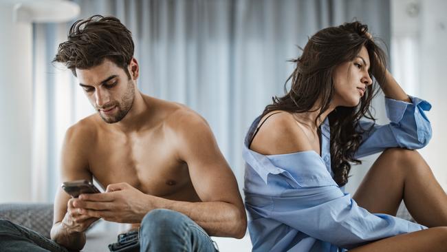 Young woman is feeling depressed while her boyfriend is text messaging on cell phone with some other woman.