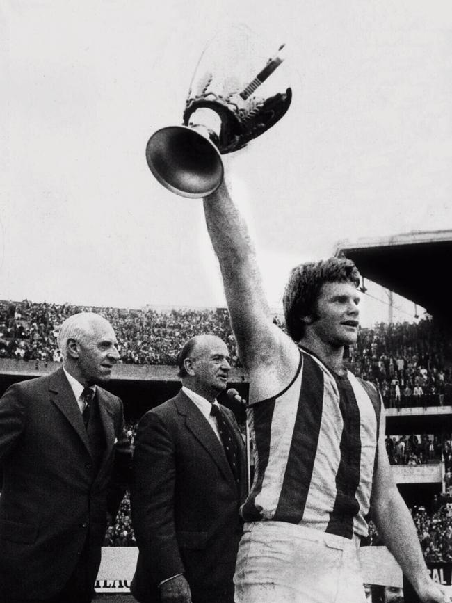 North Melbourne captain Barry Davis celebrates with the Kangaroos first ever premiership trophy, with Sir Henry Winneke and Sir Maurice Nathan in the background, in 1975.