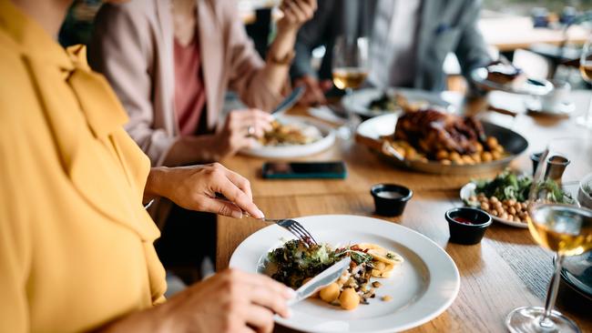 Close up of businesswoman eating lunch with colleagues in restaurant. Photo: iStock