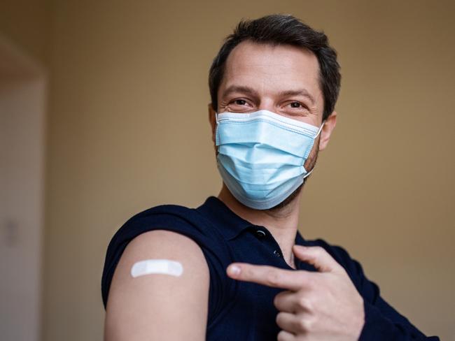 Man wearing protective face mask pointing at his arm with a bandage after receiving the covid-19 vaccine.