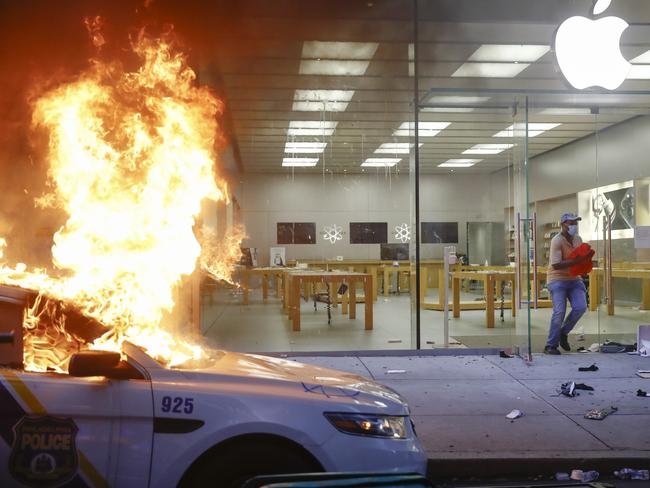 A person leaves the Apple Store as a police car burns. Picture: Matt Rourke