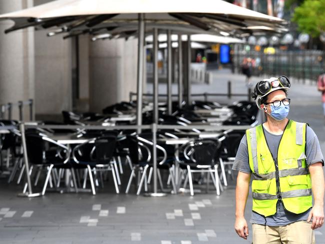 A worker with a face mask walks next to a closed restaurant along Circular Quay in Sydney on March 25, 2020, as people stay away due to restrictions to stop the spread of the worldwide COVID-19 coronavirus outbreak. (Photo by Saeed KHAN / AFP)