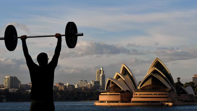 A man lifts weights in front of the Sydney Opera House at sunrise on the harbour. Picture: Joel Carrett